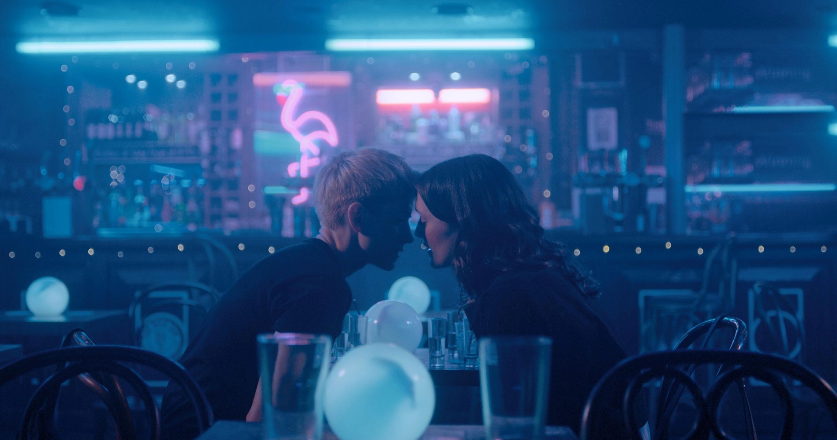 Two woman leaning into kiss in an empty bar