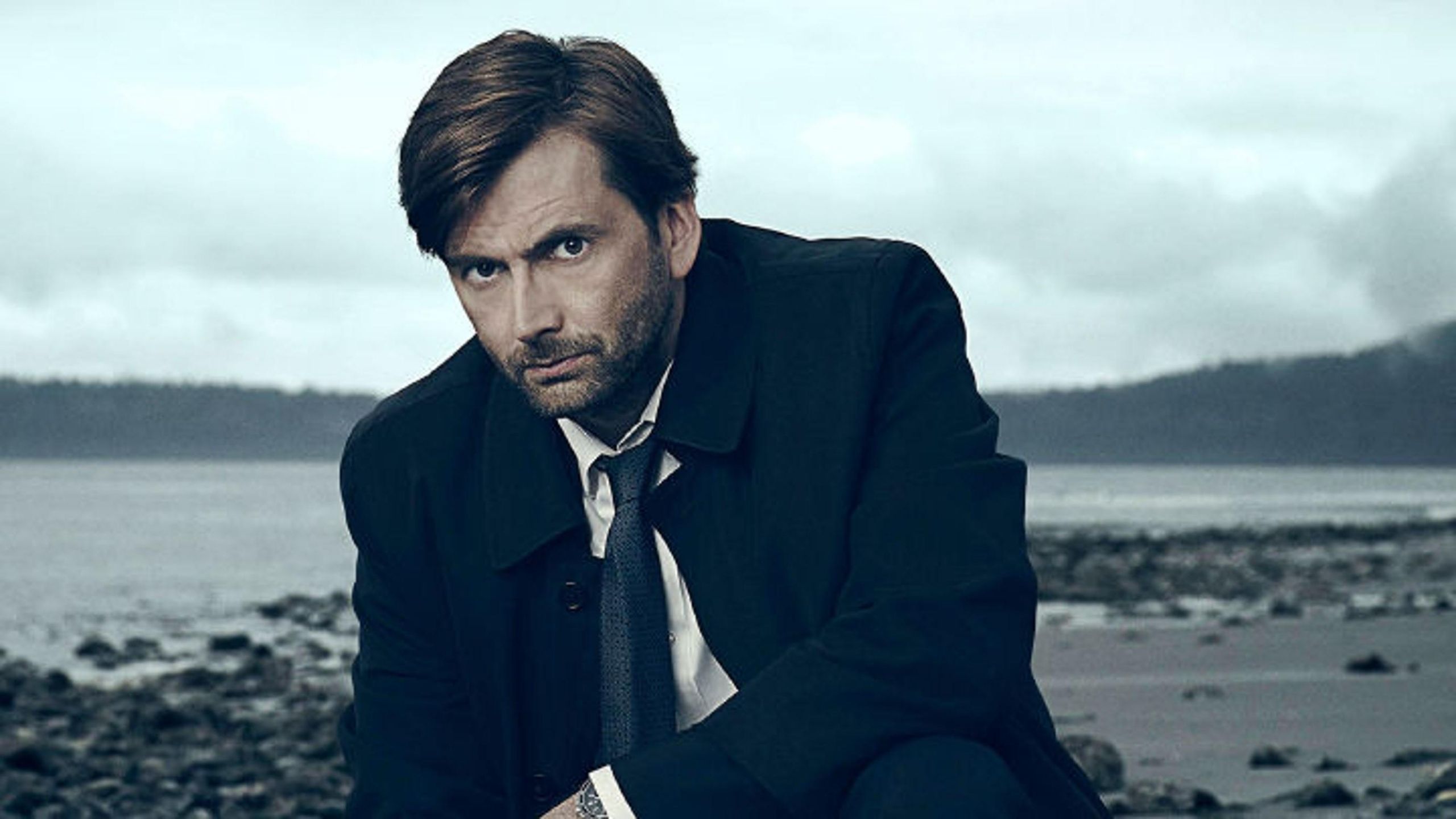 David Tenant as the main detective pictured crouching down on a beach