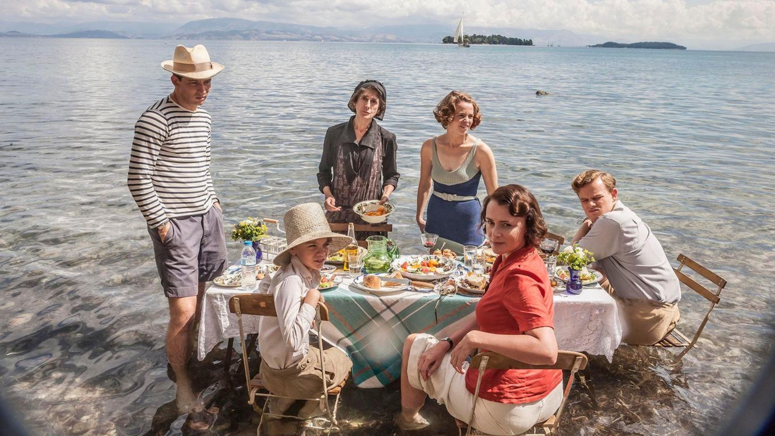 Family having lunch whilst also sat in the sea, with their table and chairs set up in the shallows of the water