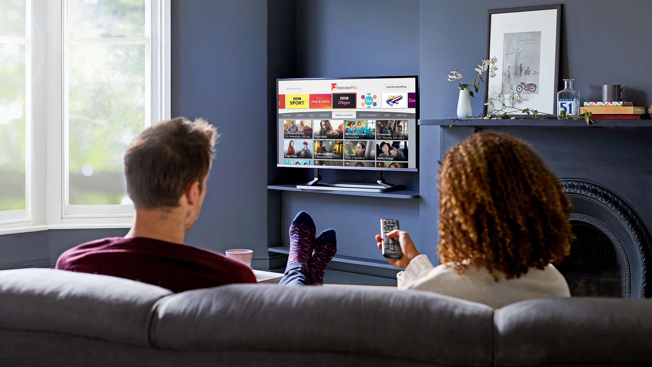 A couple sitting on a sofa watching Freeview Pla.