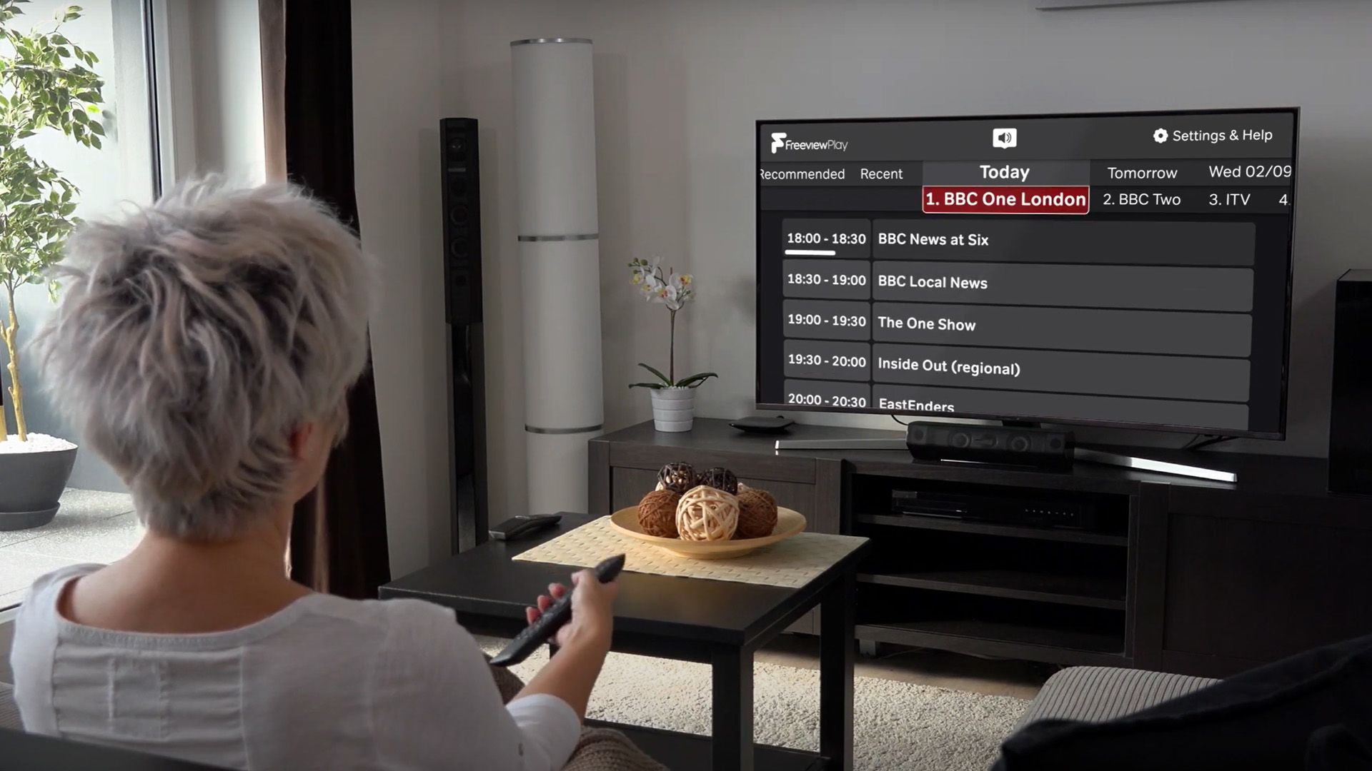 A woman holding a remote control and using the Freeview Accessible TV Guide