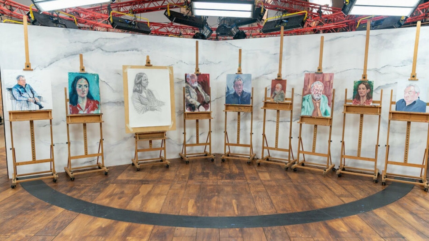 A room lined with easels, displaying painted portraits