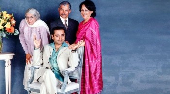 A family portrait showing a mum, dad, and a grandmother standing round a young man sat on a chair
