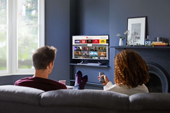 Couple looking at the Explore Freeview Play interface on their TV, about to click onto BBC Sounds