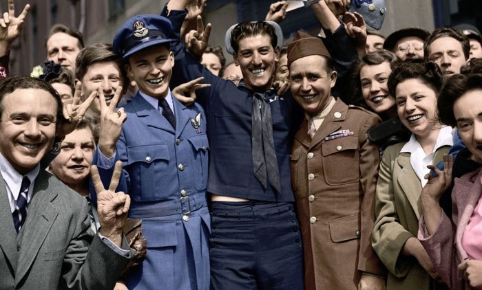 A group of smiling people making V for Victory signs with their hands on VE day in 1945