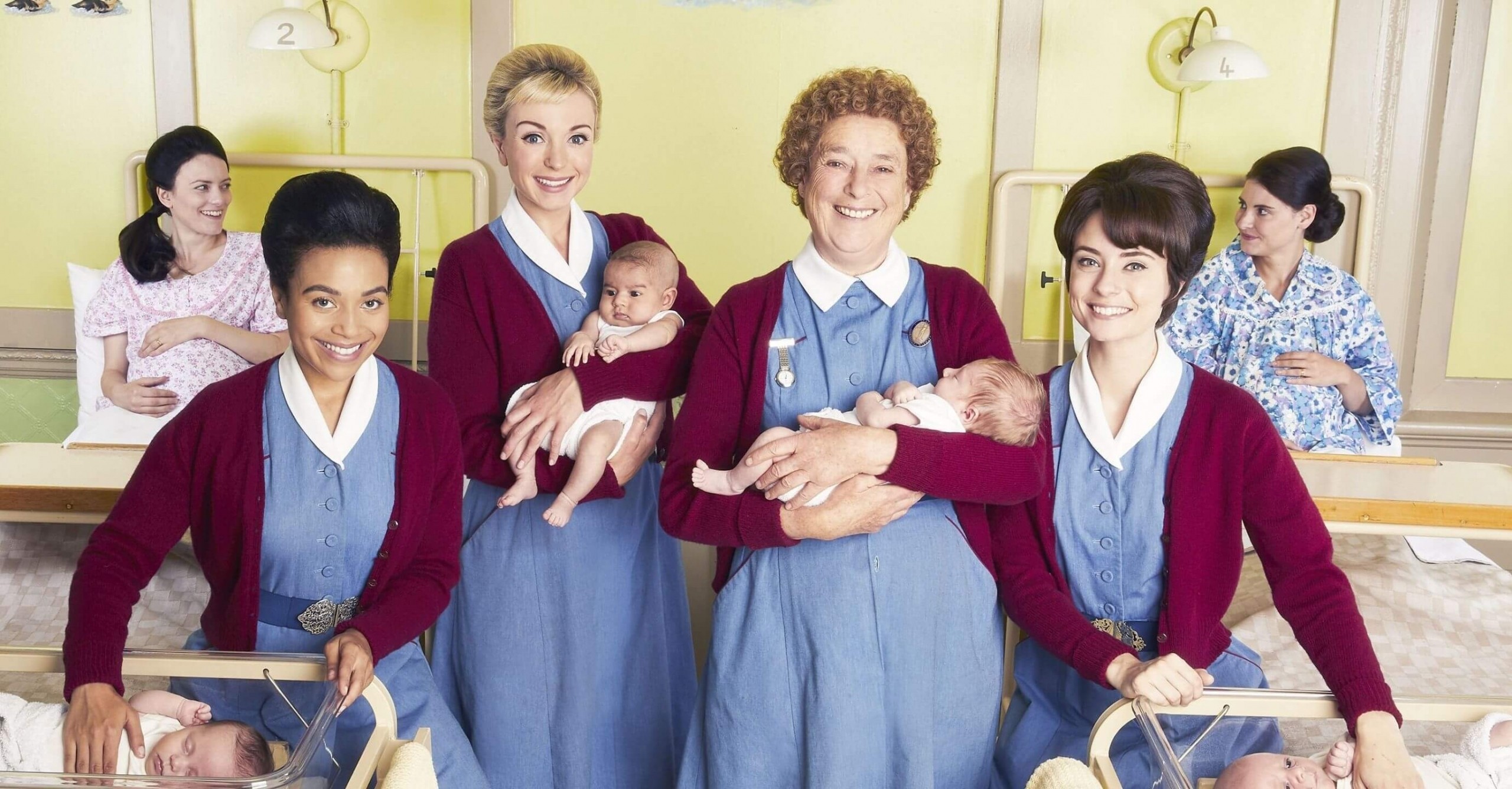 The midwives stand in a hospital ward with newly born babies smiling at the camera