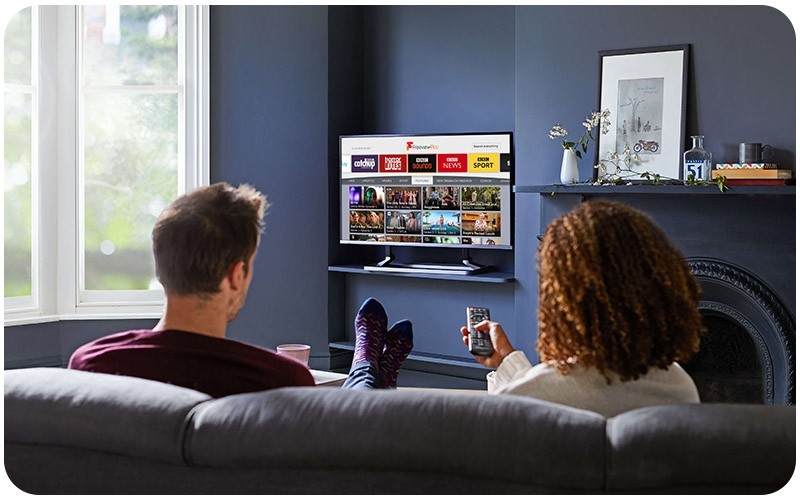 A couple seated on a sofa watching BBC Sounds on Freeview Play