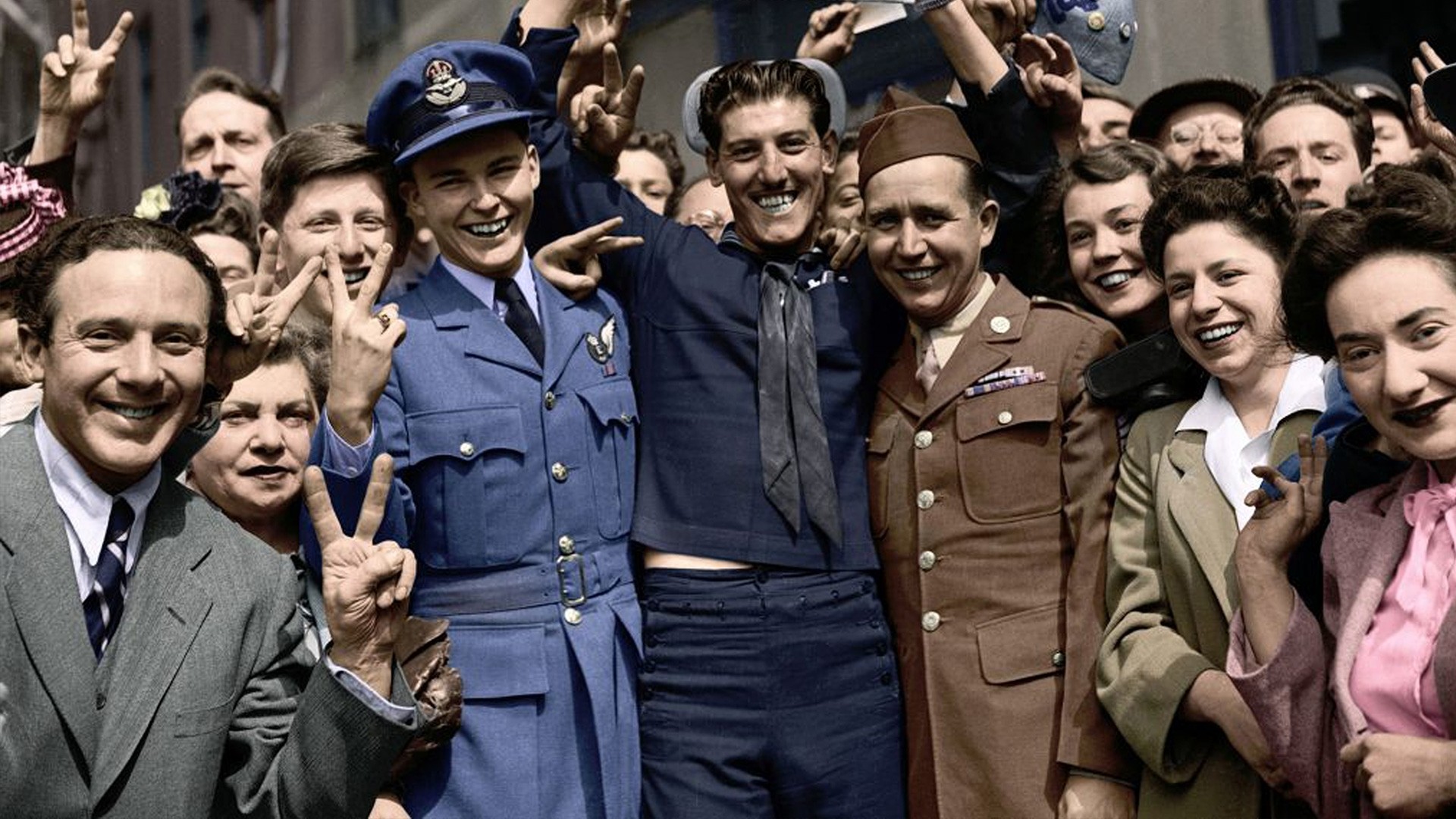 A group of smiling people making V for Victory signs with their hands on VE day in 1945