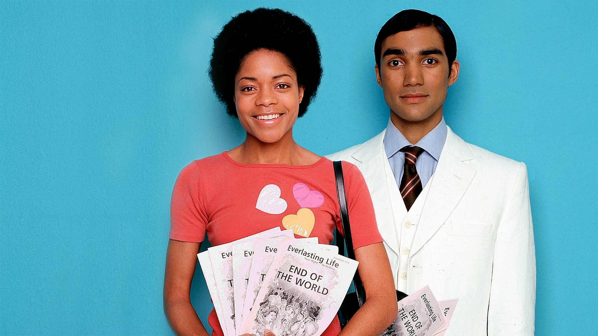 A young black woman smiling at the camera, standing in front of a smarly dressed Asian man who looks very uncomfortable