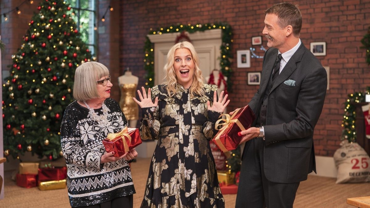 Sara Pascoe and Sewing Bee judges in festive wear stood in the sewing studio