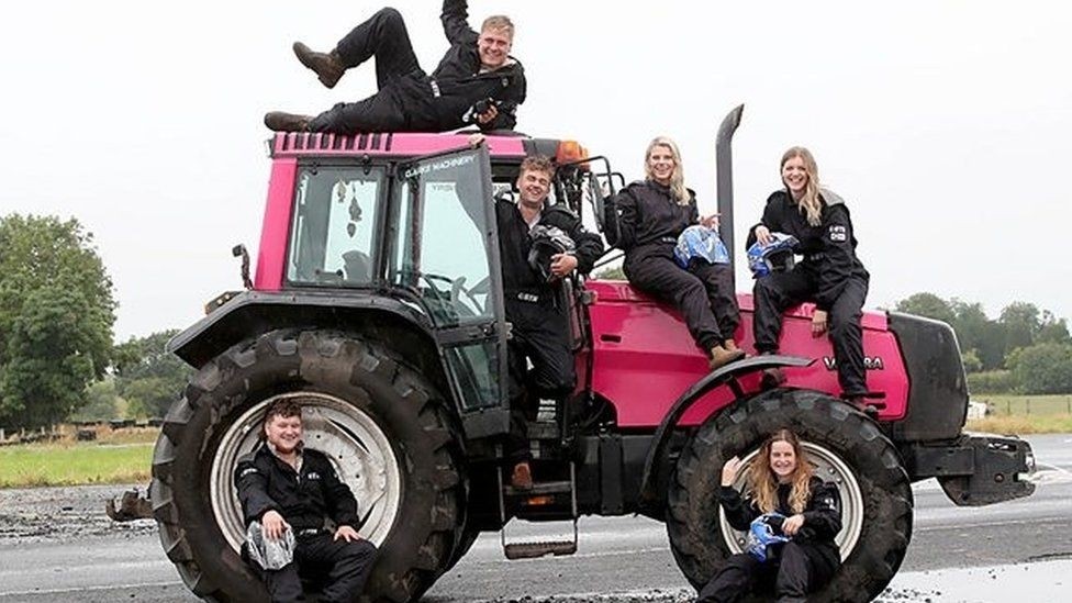 Group of young farmers all sitting on a bright pink tractor