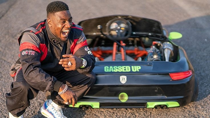 UK rapper Mist, crouching down by a racing car