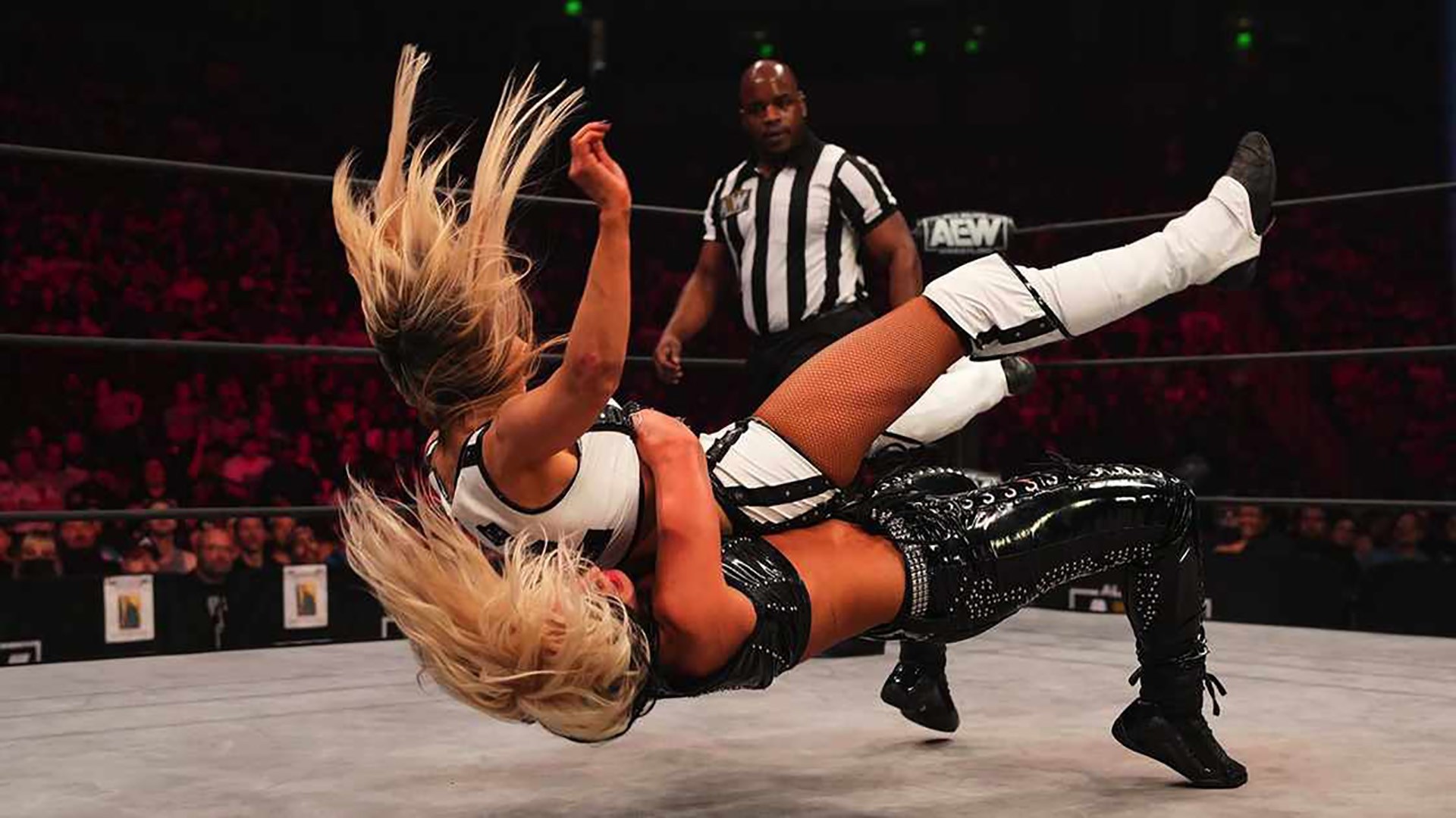 Two female wrestlers in the ring with a referee standing in the background