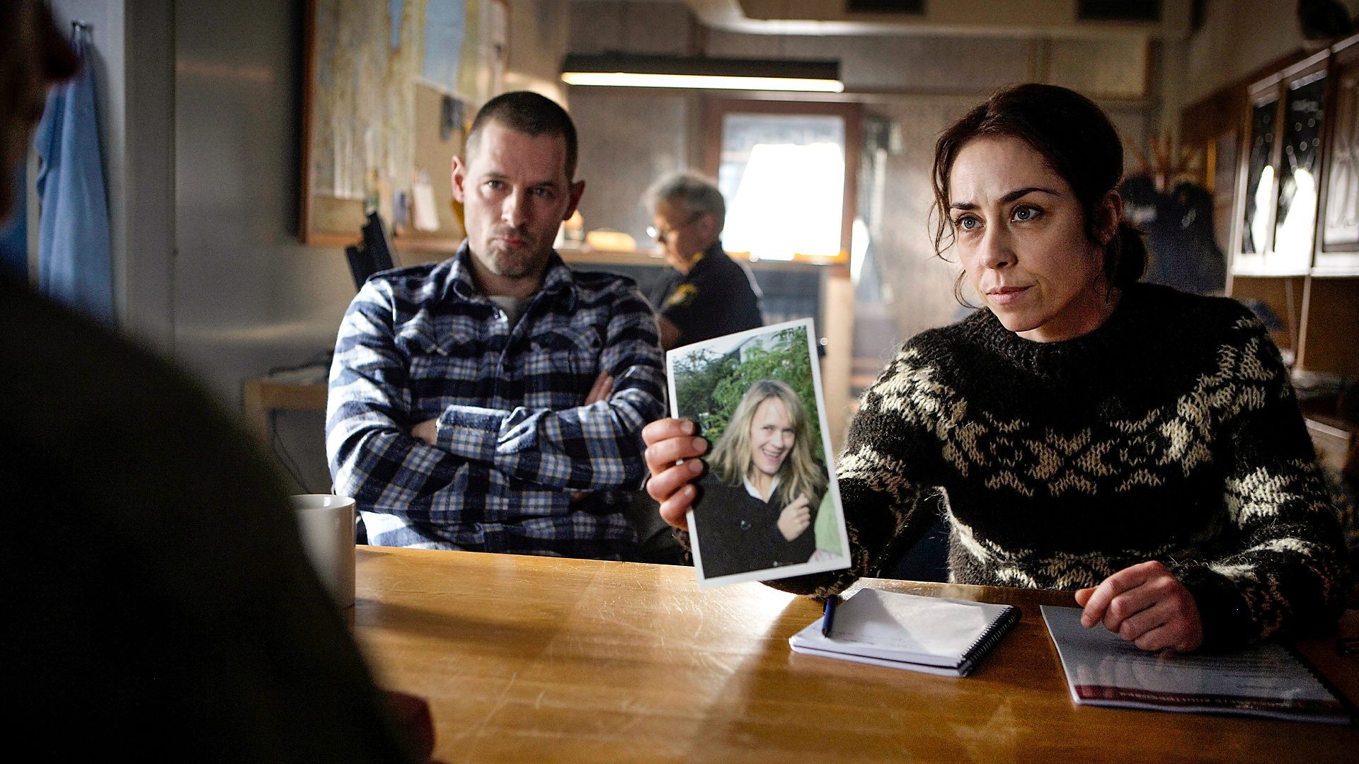 Detective Sarah Lund conducting an interview, holding a photo of a woman