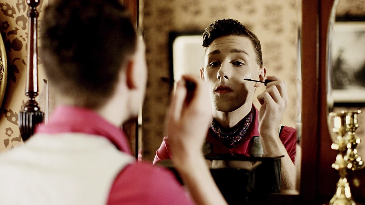 A young white man applying make up in a mirror